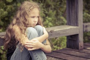 Portrait of sad blond teen girl sitting on the bridge at the day time