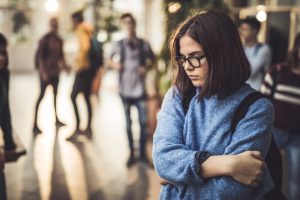 Displeased female student bullied by her classmate standing alone in a hallway.