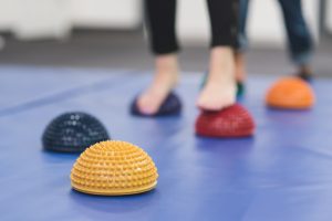 A patient is working with a physical therapist in a clinic. She is walking on sensory balls placed on a mat.