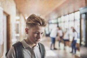 Teenage student being bullied by classmates in school. Sad boy is looking away. University students are making fun of him in corridor.